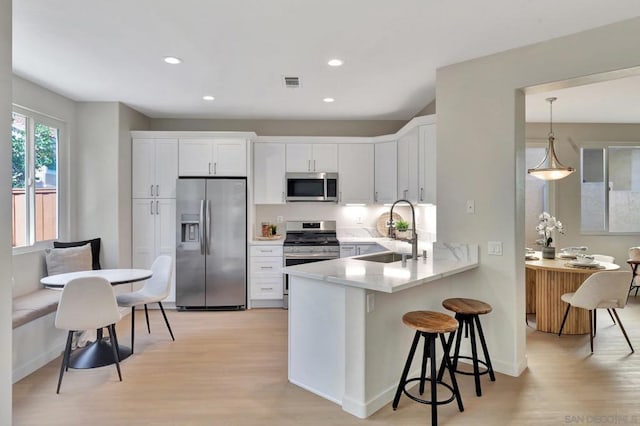 kitchen with sink, white cabinetry, appliances with stainless steel finishes, light hardwood / wood-style floors, and kitchen peninsula