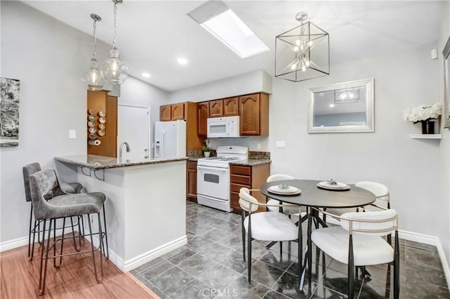 kitchen featuring lofted ceiling with skylight, a kitchen bar, kitchen peninsula, white appliances, and hanging light fixtures