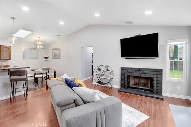 living room featuring light hardwood / wood-style flooring, a fireplace, and lofted ceiling with skylight