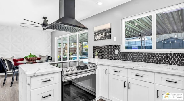 kitchen featuring electric stove, light stone countertops, wall chimney exhaust hood, and white cabinetry