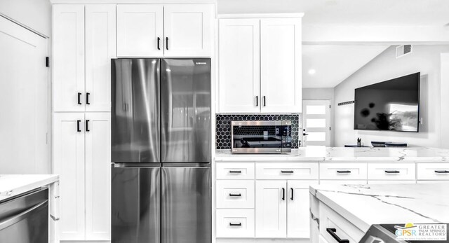 kitchen with white cabinets, appliances with stainless steel finishes, lofted ceiling, decorative backsplash, and light stone counters