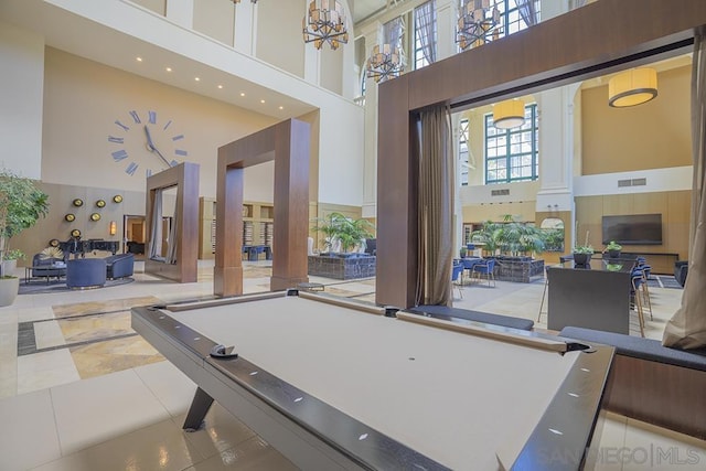 recreation room with a high ceiling, light tile patterned floors, pool table, and a notable chandelier