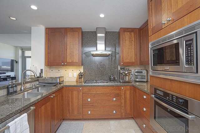 kitchen with stainless steel appliances, decorative backsplash, dark stone countertops, wall chimney exhaust hood, and sink