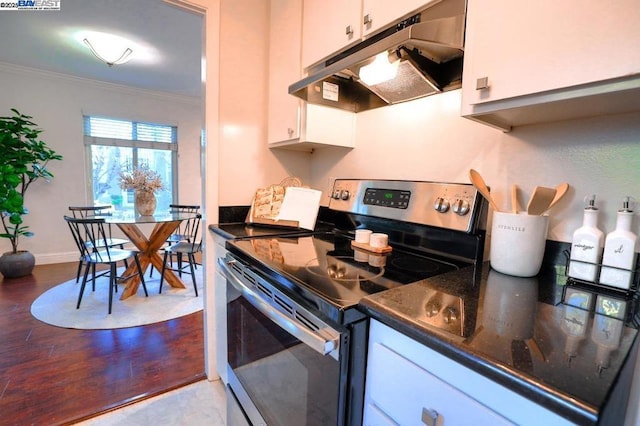 kitchen featuring white cabinetry, electric range, ornamental molding, and dark stone countertops