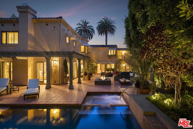 pool at dusk with an outdoor living space with a fire pit, a patio area, and an in ground hot tub