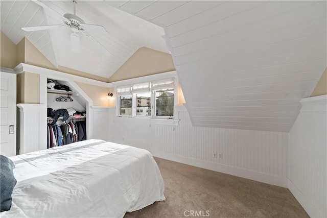 bedroom featuring lofted ceiling, ceiling fan, wood walls, light carpet, and a closet