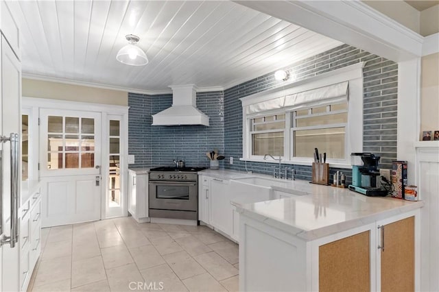 kitchen featuring custom exhaust hood, sink, white cabinetry, stainless steel range, and light tile patterned floors