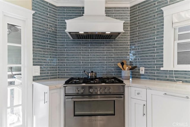 kitchen with tasteful backsplash, white cabinets, stainless steel range, and premium range hood