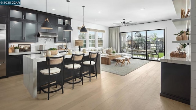 kitchen featuring a kitchen bar, ceiling fan, a kitchen island with sink, decorative light fixtures, and light hardwood / wood-style flooring