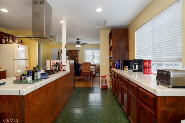 kitchen with tile counters, ceiling fan, white refrigerator, and island exhaust hood