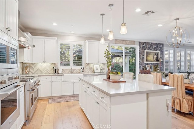 kitchen with pendant lighting, appliances with stainless steel finishes, a kitchen island, white cabinetry, and tasteful backsplash