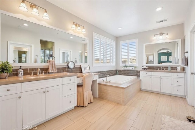 bathroom featuring tiled bath, decorative backsplash, and vanity