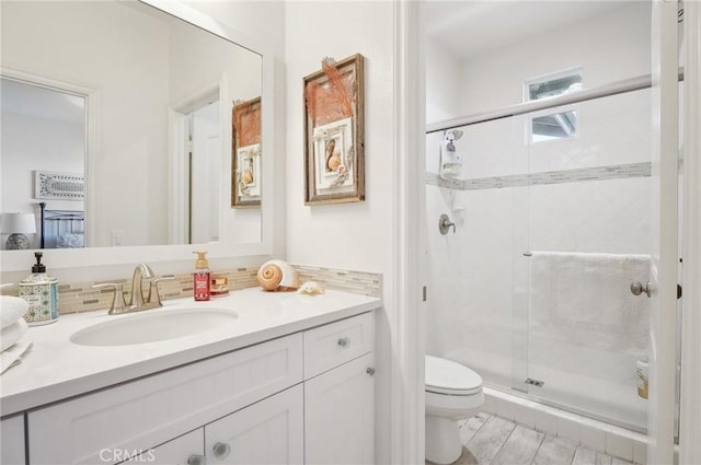 bathroom featuring toilet, decorative backsplash, a shower with door, and vanity