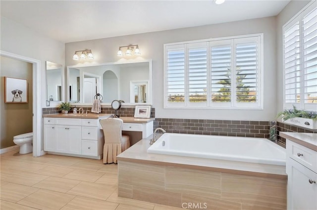 bathroom with vanity, toilet, plenty of natural light, and a relaxing tiled tub