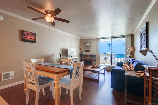 dining space featuring ceiling fan, a tile fireplace, crown molding, a textured ceiling, and a wall of windows