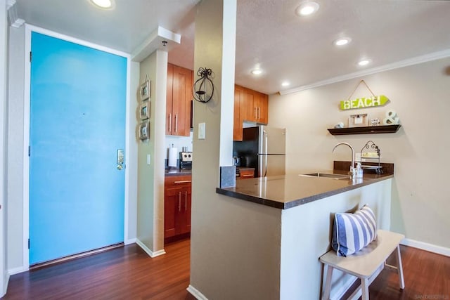 kitchen with kitchen peninsula, sink, crown molding, dark hardwood / wood-style flooring, and stainless steel fridge