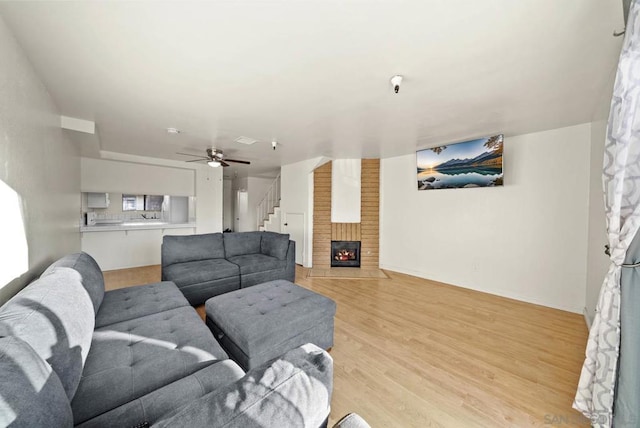 living room featuring light wood-type flooring, ceiling fan, and a fireplace