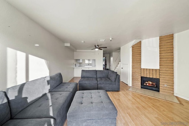 living room featuring ceiling fan, light wood-type flooring, and a fireplace