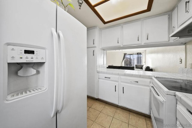 kitchen featuring light tile patterned flooring, tile countertops, white cabinetry, and white appliances