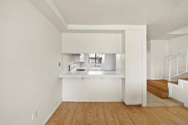 kitchen featuring tile countertops, light hardwood / wood-style flooring, white electric range oven, stainless steel refrigerator, and white cabinets