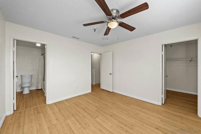 unfurnished bedroom with a textured ceiling, a closet, light wood-type flooring, ceiling fan, and ensuite bathroom