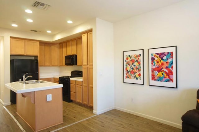 kitchen with black appliances, wood-type flooring, an island with sink, sink, and a kitchen breakfast bar