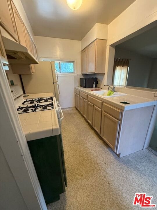 kitchen with tile countertops, light brown cabinetry, white gas range oven, and sink