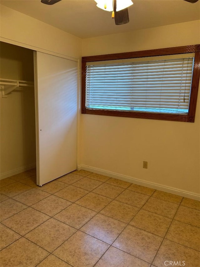 unfurnished bedroom with a closet, light tile patterned floors, a ceiling fan, and baseboards