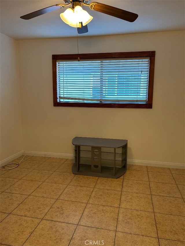 empty room with light tile patterned flooring, a healthy amount of sunlight, a ceiling fan, and baseboards