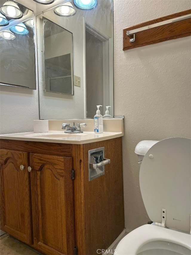 bathroom featuring toilet, vanity, and a textured wall