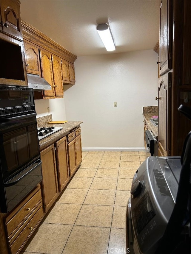 kitchen with light tile patterned floors, baseboards, oven, under cabinet range hood, and a warming drawer