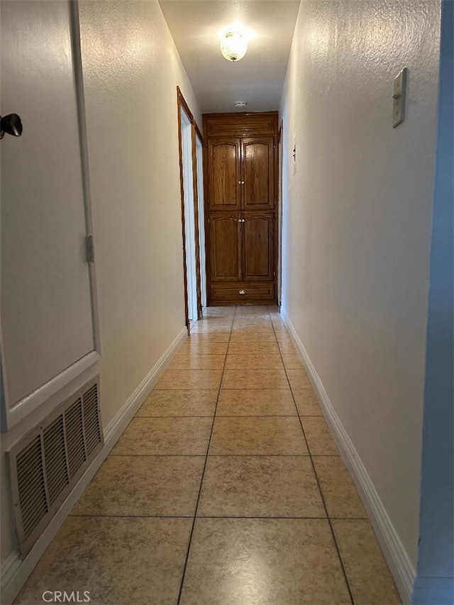hall with visible vents, baseboards, and light tile patterned floors
