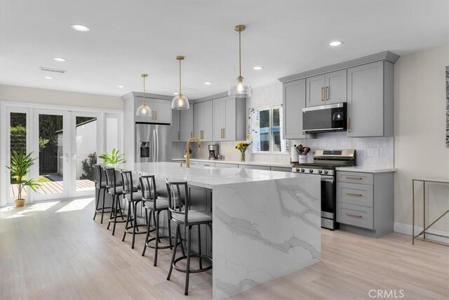 kitchen with a center island with sink, gray cabinets, stainless steel appliances, pendant lighting, and sink