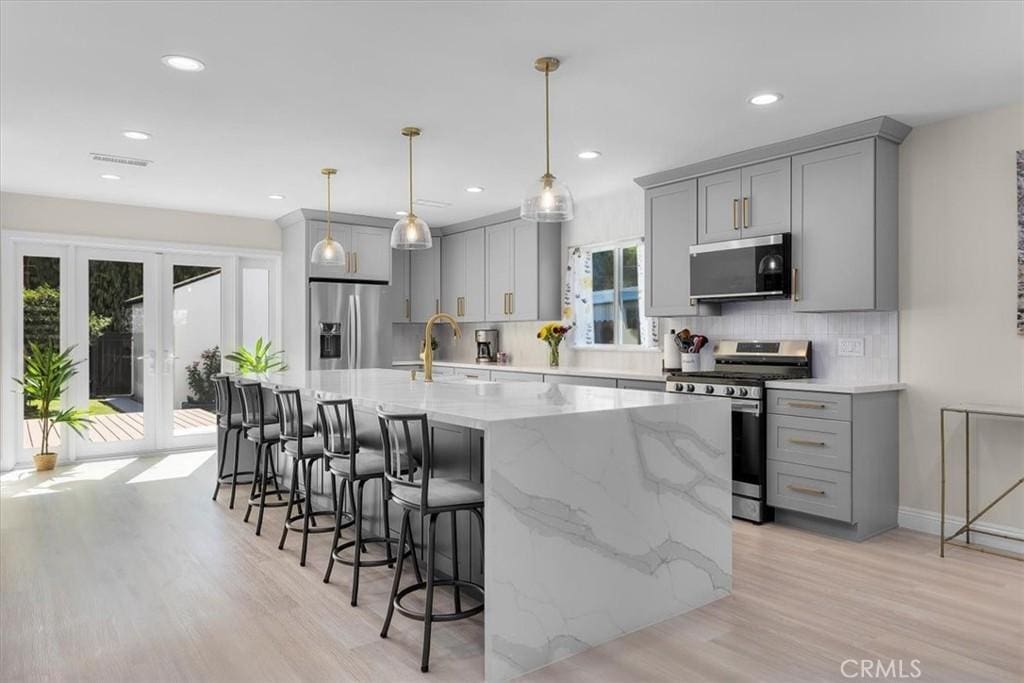 kitchen featuring a center island with sink, pendant lighting, sink, gray cabinetry, and stainless steel appliances