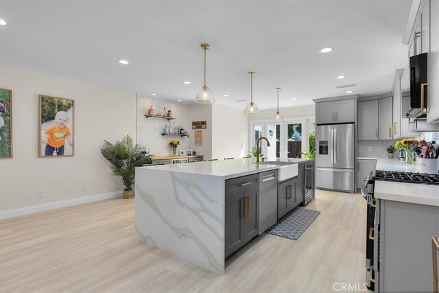 kitchen featuring pendant lighting, appliances with stainless steel finishes, gray cabinets, and an island with sink