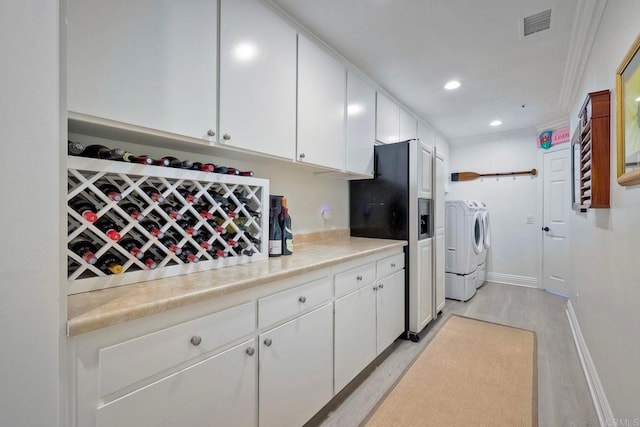 kitchen with washer and dryer, refrigerator with ice dispenser, white cabinets, crown molding, and light wood-type flooring