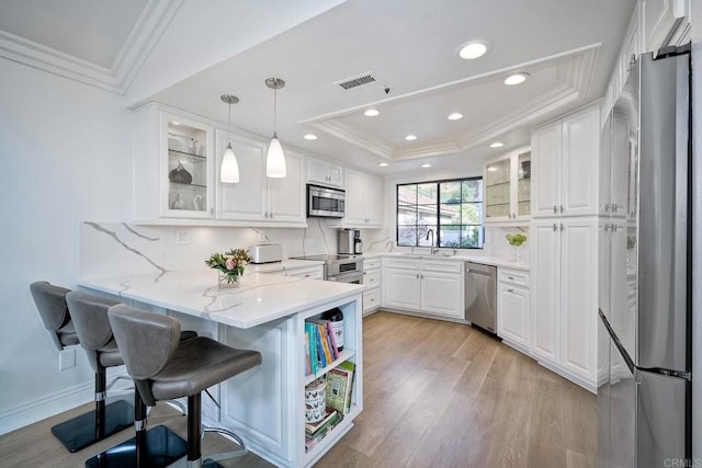 kitchen featuring white cabinets, decorative backsplash, hanging light fixtures, kitchen peninsula, and stainless steel appliances