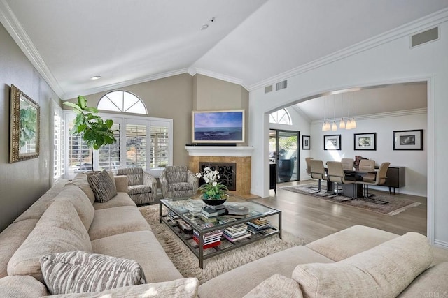 living room with wood-type flooring, lofted ceiling, ornamental molding, and a fireplace