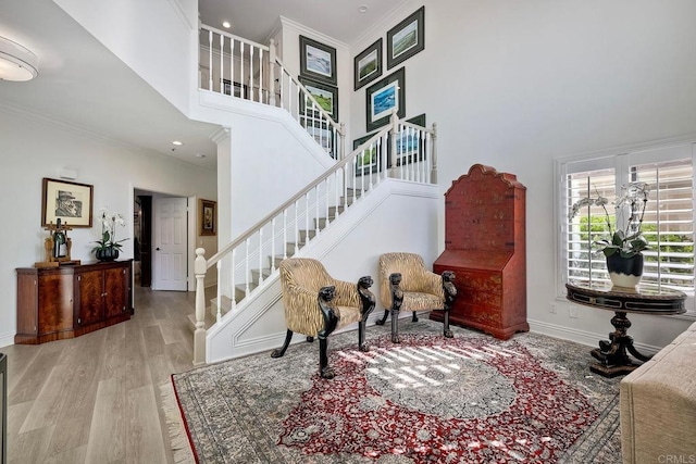 sitting room with ornamental molding, a towering ceiling, and light wood-type flooring