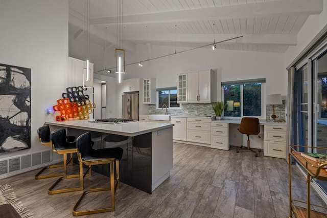 kitchen featuring white cabinetry, hardwood / wood-style floors, appliances with stainless steel finishes, decorative backsplash, and beamed ceiling