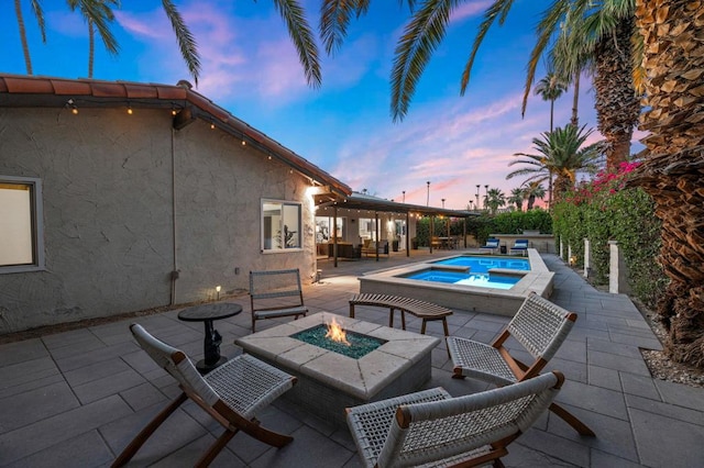 pool at dusk featuring a patio area, an in ground hot tub, and a fire pit