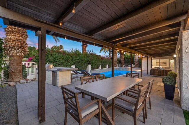 patio terrace at dusk with a fenced in pool, an outdoor kitchen, and a bar