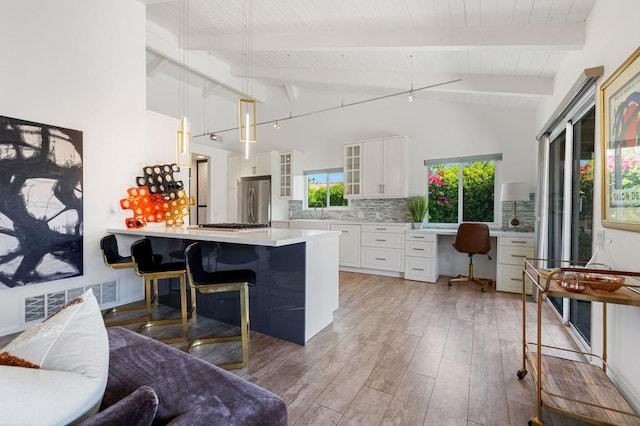 kitchen featuring white cabinetry, hanging light fixtures, stainless steel refrigerator, a breakfast bar, and beam ceiling