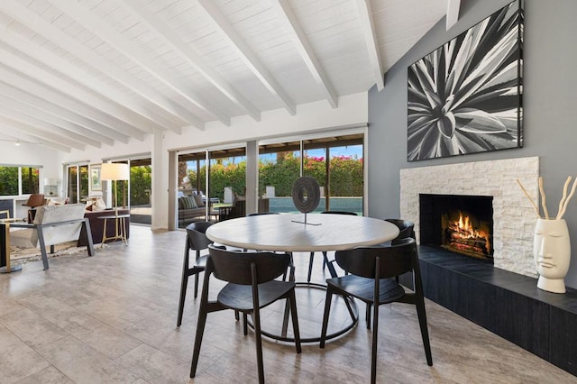 dining space featuring a stone fireplace and vaulted ceiling with beams