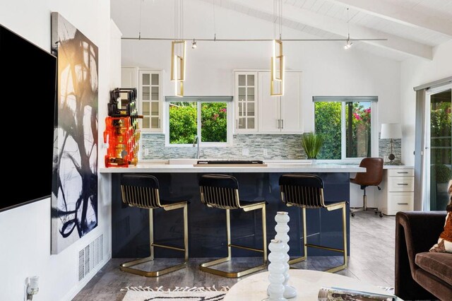 kitchen with pendant lighting, white cabinets, tasteful backsplash, vaulted ceiling with beams, and a breakfast bar