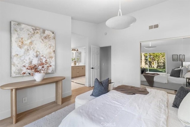 bedroom featuring light wood-type flooring, ensuite bathroom, and a high ceiling