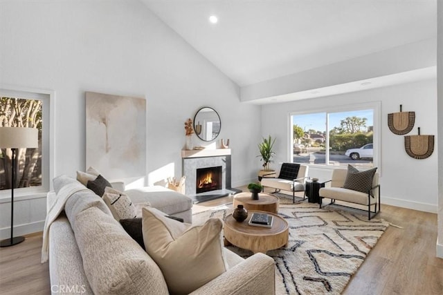 living room with high vaulted ceiling, a high end fireplace, and light wood-type flooring