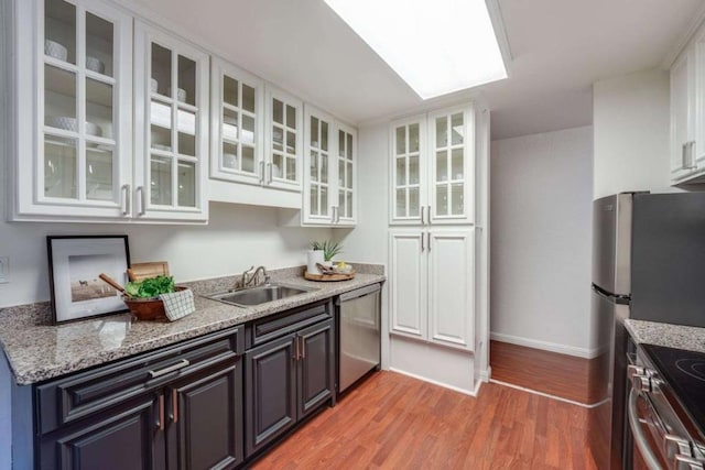 kitchen with sink, light hardwood / wood-style flooring, light stone countertops, white cabinetry, and stainless steel appliances