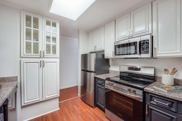 kitchen with a skylight, light stone countertops, white cabinetry, stainless steel appliances, and light hardwood / wood-style flooring