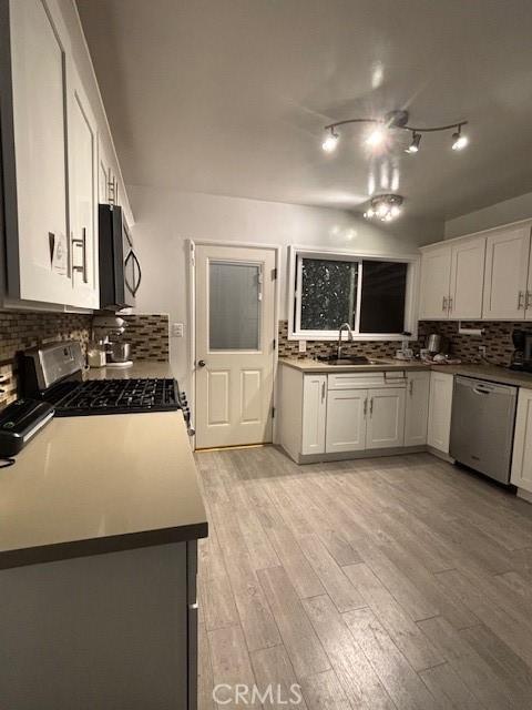 kitchen with range, white cabinetry, sink, stainless steel dishwasher, and light hardwood / wood-style flooring